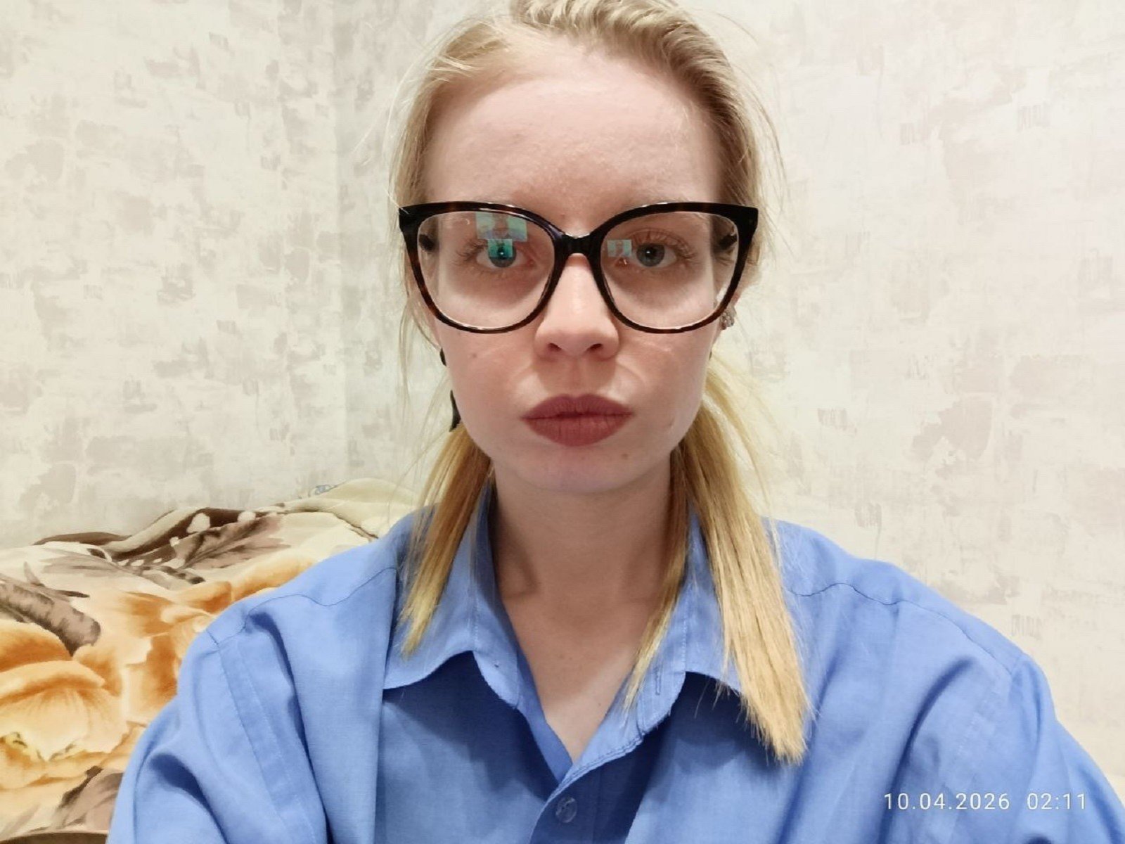 TemekaTrick with blonde hair, black glasses, and pouty lips, wearing a blue shirt, has a serious expression, and a date stamp in the bottom right.