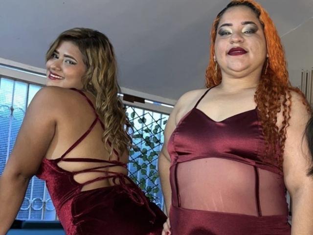 Two SecretFroomies in maroon velvet dresses with sheer panels. One has curly brown hair, smiling, showing her ass. The other has red curly hair, dark lipstick, and a chubby face.