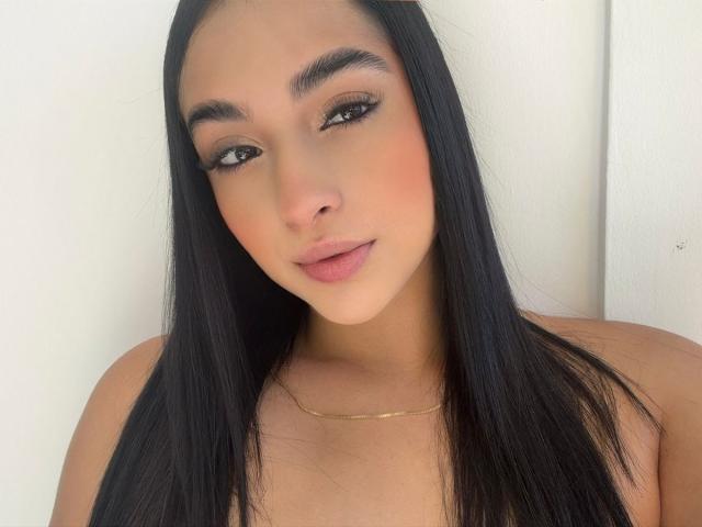 EmmaWaltter has long black hair, brown eyes, and full pink lips. She's wearing a gold necklace and has a soft, sexy, attractive face with subtle makeup.