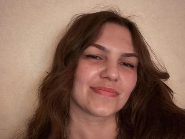 Kalipso69 has messy brown hair, light skin, and a slightly smug smile with pink lips, showing a few freckles and a small blemish on her right cheek.