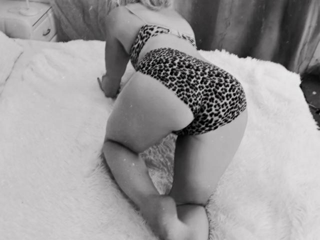 LorraSchmidt is on all fours on a fluffy bed, wearing leopard print panties and a matching top, showing her ass and curvy butt. Black-and-white photo.