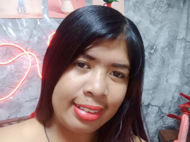 MariahSquirting69 has shiny black hair, brown eyes, red lipstick, and a slight nose piercing. Neon light outlines her face. She's smiling with her pink lips slightly parted.