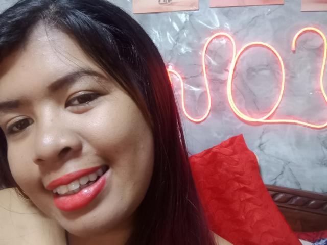 MariahSquirting69's smiling face with red lipstick, black hair, and slightly glossy skin. Neon red "2022" in background, red pillow in bottom right.