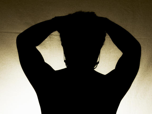 Silhouette of AdoniBaskerville with arms raised, hands behind head, dark against a bright background. AdoniBaskerville's hair is visible, but face and body are completely black.