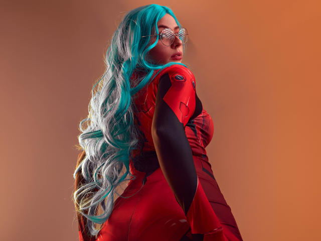 VanessaClose with long teal-blue wavy hair, wearing a red and black futuristic outfit, looking over her shoulder, glasses on, orange background, tight red dress, sexy, butt visible.
