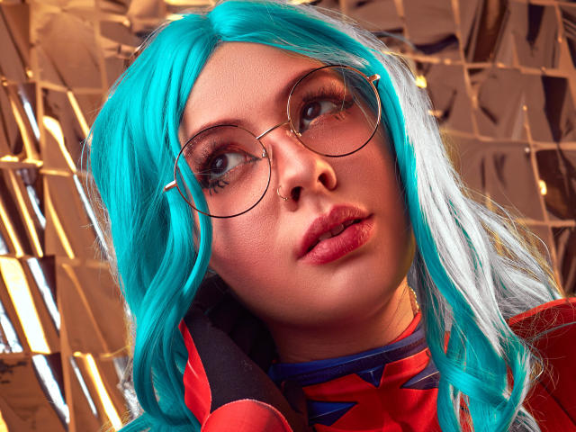 VanessaClose with teal hair, round glasses, and red lipstick, looking up with a slight pout, wearing a red and blue outfit, has a cute nose and soft skin.