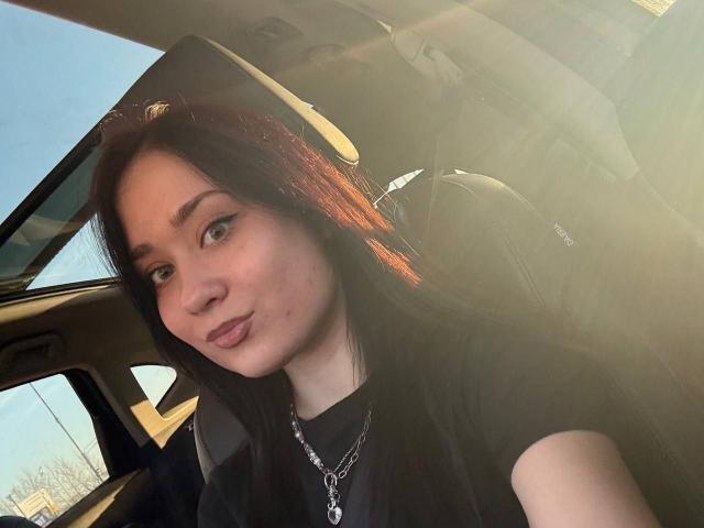 PatienceObremski has long dark hair, pouty lips, and a chain necklace, sitting in a car with sunlight, looking at the camera with a slight smirk.