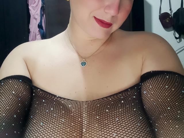 AlexaHotSeins with red lipstick, wearing a black fishnet top, showing her tits, necklace with a blue heart, and no bra, in a selfie. Her tits are visible through mesh.