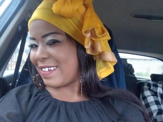Una donna con un foulard giallo, un vestito nero e orecchini d'argento, sorride in macchina, mostrando denti bianchi, sopracciglia scure e lunghi capelli neri. Il suo seno non è visibile..