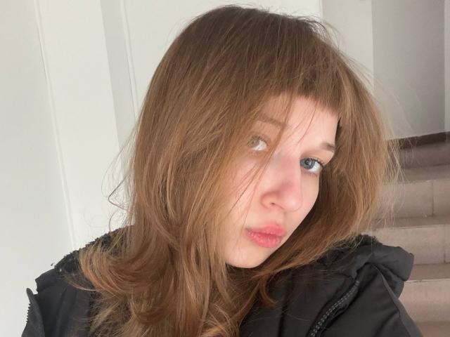 FerminaHilmer has light brown, slightly messy hair covering her eyes, pale skin, and wears a black jacket. She looks tired with pink, slightly parted lips.