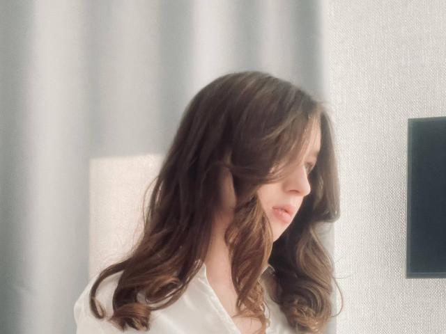 Sara Rosenbarger tiene el pelo castaño ondulado, labios rosados suaves y una camisa blanca, mirando hacia la derecha con una expresión gentil y pacífica. Su rostro está ligeramente desenfocado..