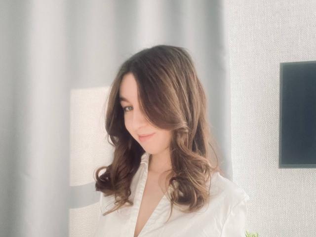 Sara Rosenbarger ha i capelli castano ondulati, un sorriso carino, e indossa una camicia bianca con un leggero taglio a V, che lascia intravedere un po' il suo seno. L'illuminazione è soffusa..