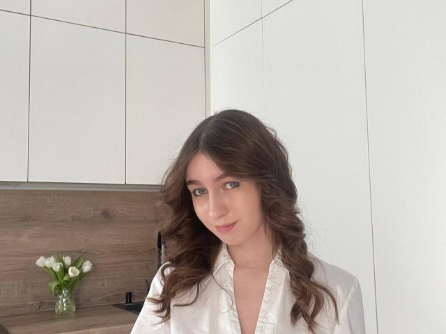Sara Rosenbarger mit welligem, braunem Haar, die ein weißes Hemd mit Knopfleiste trägt und sanft lächelt, in einer hellen Küche mit weißen Schränken und einer Holzrückwand, hält einen Strauß weißer Tulpen..
