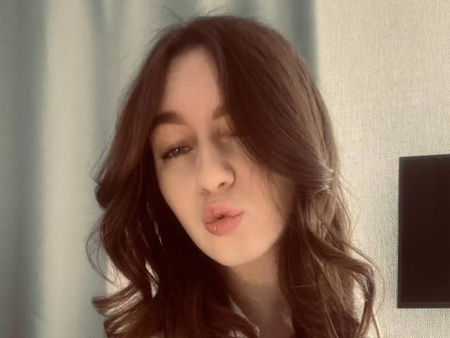 Sara Rosenbarger ha i capelli castano ondulati, labbra rosa carnose e un viso carino, con lo sguardo leggermente di lato e la luce soffusa del sole che mette in risalto i suoi lineamenti..