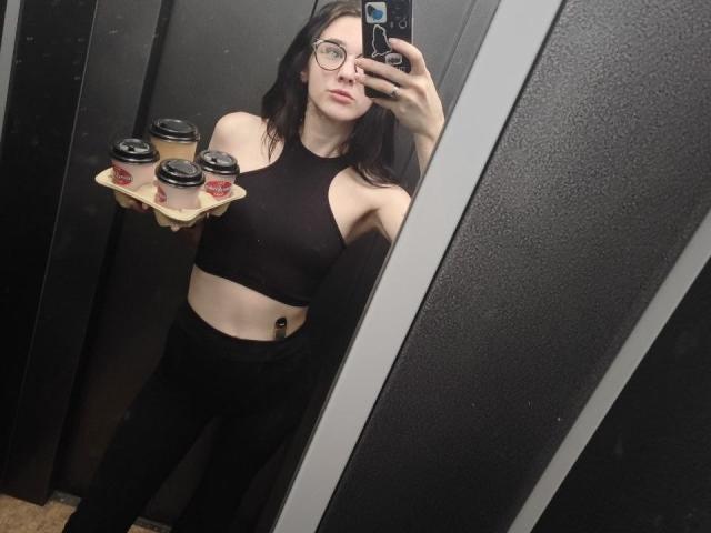 NatoshaBurdine with black hair, glasses, holding tray with coffee cups, wearing black sports bra and pants, taking mirror selfie, showing slim midriff with small tattoo.