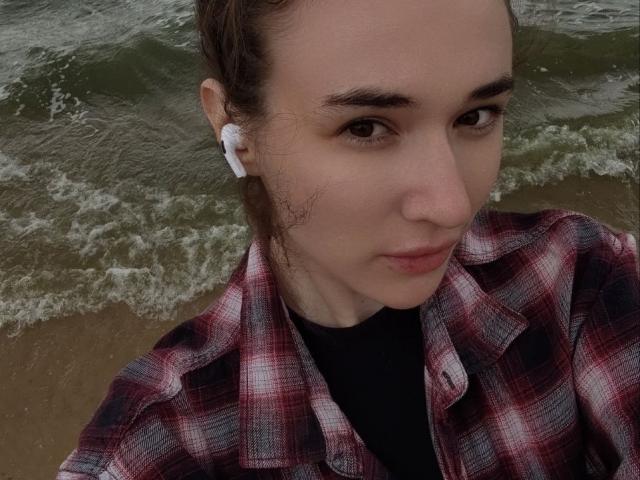 NatoshaBurdine has a fair skin tone, brown eyes, and is wearing a red plaid shirt with black earbuds. Her brown hair is tied back. Her small nose is visible.