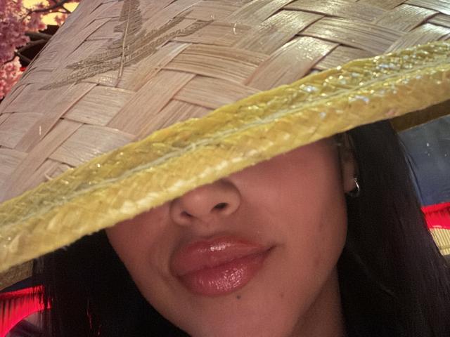 MajoJones with a straw hat covering her eyes, has glossy red lips, and a small beauty mark on her upper lip. Her black hair is partially visible.