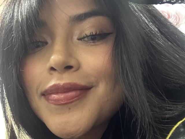MajoJones has dark brown eyes with black eyeliner, full pink lips, and medium brown skin. She's smiling slightly, with black straight hair covering her right eye.