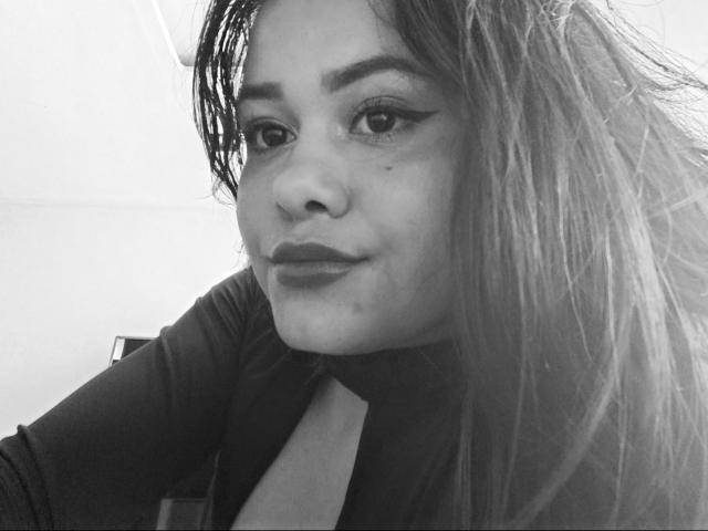 Black-and-white selfie of JennLunaLee with long, wet, messy hair, winged eyeliner, dark lipstick, and a slight smile, wearing a high-neck, dark top. Her nose has a small blemish.