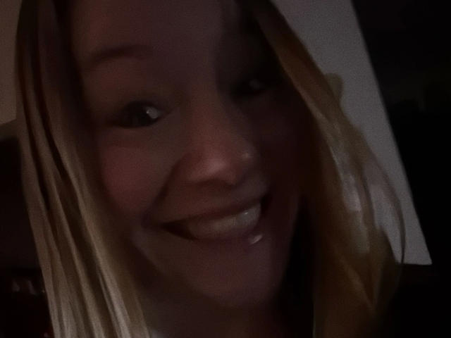 Anna89-hot heeft blond haar, een licht verlicht gezicht en een brede, tandrijke glimlach waarbij haar glanzende tanden te zien zijn. Haar ogen zijn licht geopend en haar huid is bleek..