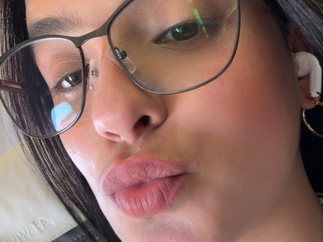 MaiaPark's pouty pink-ass lips, wearing thick glasses, with white earbuds, brown hair, and light skin, reflected in a mirror. Her brown eyes and subtle makeup are visible.