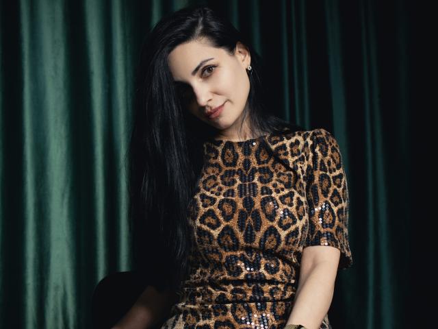 BeatriceLovely with long black hair, wearing a leopard print dress with sequins, smiling slightly, looking at camera, green velvet curtain in background, cute and sexy.