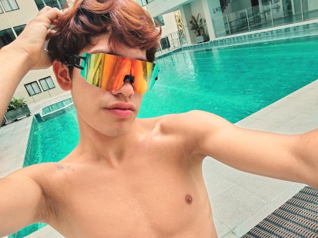 JacobeLord with orange reflective sunglasses, shirtless, brown wavy hair, hand in hair, by the blue pool, showing a small tattoo on right shoulder, looking at camera.