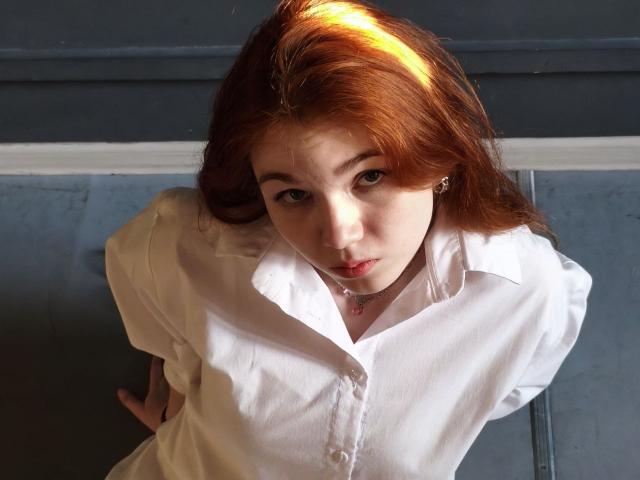 KatiRokisky with red hair, wearing a white button-up shirt, looking up with a slightly curious expression, sunlight in her hair, hands on her back, soft light on her face.