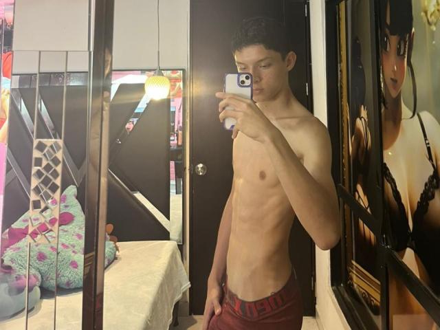 SamuJasper, shirtless, with a slim, toned, and smooth chest, wearing red underwear, taking a mirror selfie, holding a phone, black hair, standing in a bedroom.