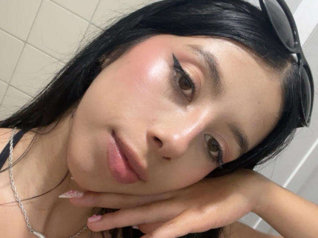 LanaKingsley has a cute face with black hair, brown eyes, and thick black eyeliner. Her pink cheeks and glossy lips are visible. She's resting her chin on her hand.