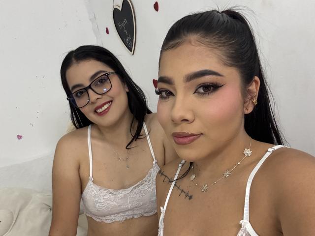 KymAndNala with glasses and white lace bra, and KymAndNala with makeup, pink lipstick, and white lace bra, showing small tits and tattoos, in selfie.