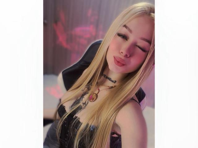MiaValenttine with long blonde hair, closed eyes, pouty lips, black lace dress, tattoos, necklace, and a black jacket, looking cute and sexy.