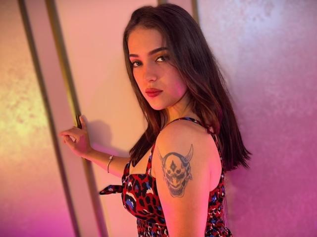 KatarinaNovak with dark brown hair, wearing a leopard print dress, holding a cigarette, showing a skull tattoo on her right arm, pink and purple lighting.