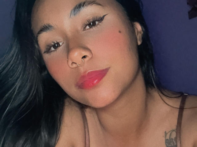 AnaRome tiene una piel marrón media, cabello negro largo, cejas pobladas, un piercing en la nariz, lápiz labial rojo y una pequeña peca en su mejilla derecha. Su tatuaje es parcialmente visible..