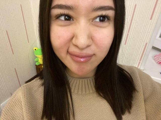 IzettaDingel has a cute smile, shiny pink lips, and long straight brown hair, wearing a beige knit sweater. Her brown eyes are looking slightly to the side.