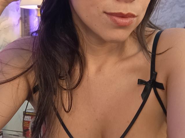 MiaReed's face and chest, showing her lips with pinkish lipstick, and her black strappy lingerie with small black bows on her tits. Her brown hair is partially visible.