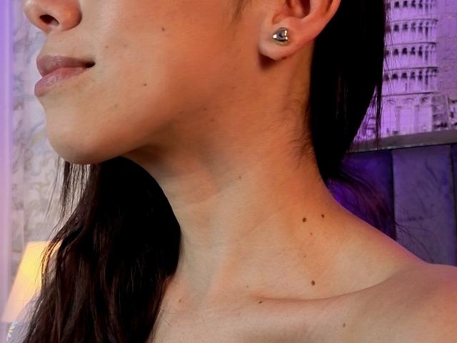 MiaReed's face, focusing on her smooth neck and upper chest with a small, dark mole near her collarbone, wearing a single, small, silver stud earring in her left ear.