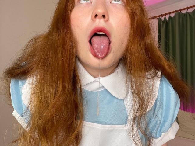 GingerCutie with red hair, tongue out, drooling, wearing a blue and white dress, looking up. Saliva hanging from her tongue. Her eyes are half-closed, looking up.