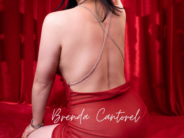 BrendaCantorel in a red dress, back to camera, showing bare back and silver chain necklace, sitting on red fabric, her ass slightly visible.