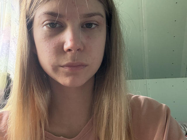 Danae Egger hat langes, blondes Haar, blasse Haut und einen leicht schmollenden Gesichtsausdruck, wobei dünne Haarsträhnen über ihr Gesicht hängen. Sie trägt ein rosa Hemd..