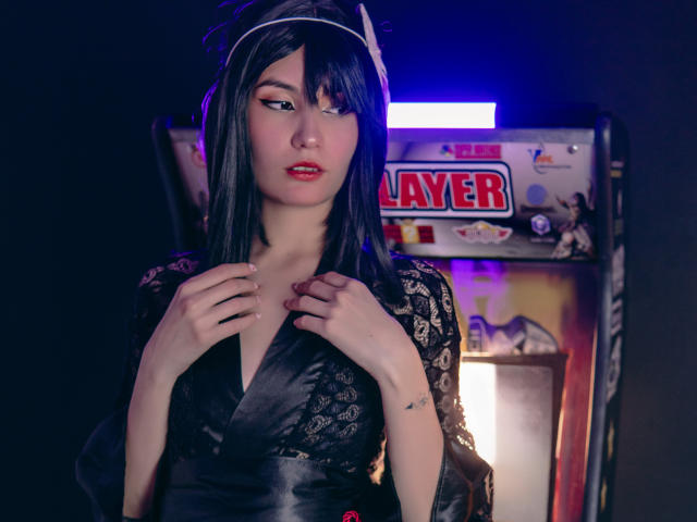 LilaLaurent with black lace kimono, pale skin, red lipstick, and straight dark hair, hands on chest, looking down, neon blue light in background, subtle tattoo on right wrist.