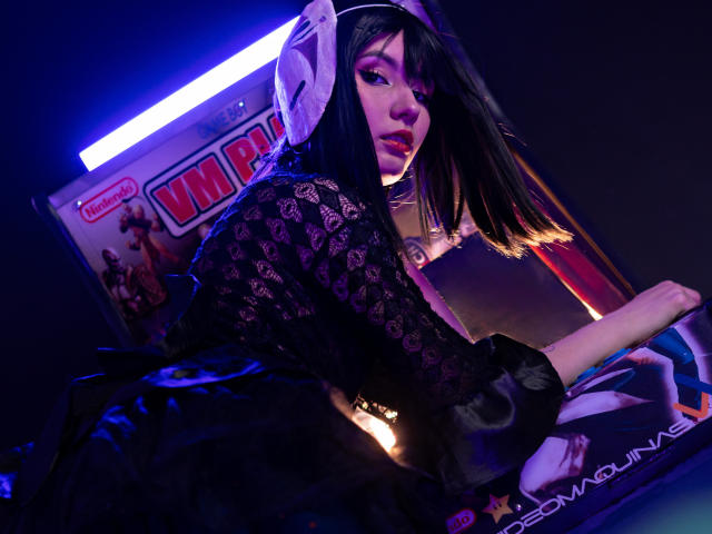 LilaLaurent with black lace dress, white headphones, and long dark hair, looking back with a seductive gaze, purple neon light in background, sitting on a gaming chair.
