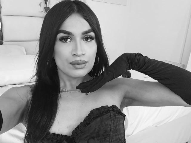 SilvanaCastro with dark, straight hair, wearing black lace top, black gloves, and hoop earrings, pouting with her hand on her neck, in a black-and-white selfie.