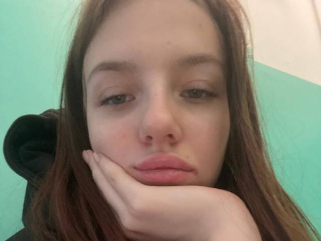 DignaHottie ha la pelle chiara, gli occhi marroni e le labbra rosa, con i capelli castani e una mano appoggiata sulla guancia, con un'espressione leggermente annoiata o pensierosa..