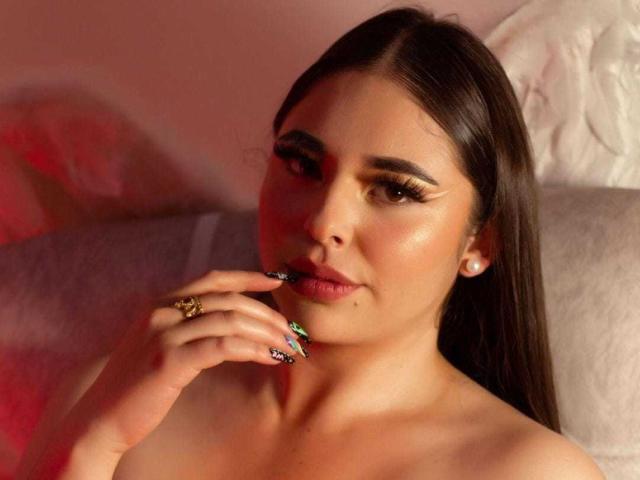 BaGiolett hat dunkelbraunes Haar, volle Augenbrauen und lange Wimpern. Sie berührt ihre Lippen mit bunten, glitzernden Nägeln, trägt einen Ring und Perlenohrringe und wirkt verführerisch..
