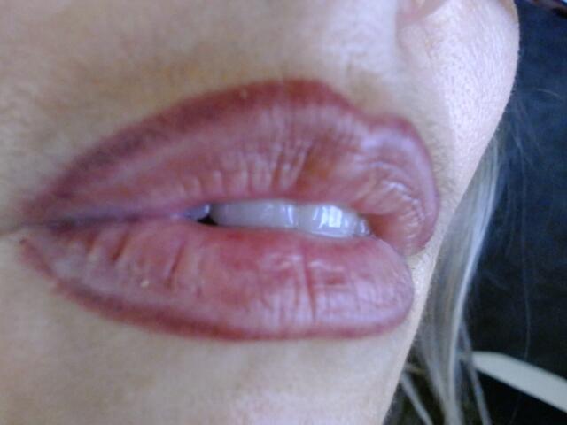 Os lábios carnudos e levemente entreabertos de VickySexyFr, com batom rosa avermelhado brilhante, mostrando um pequeno vislumbre de dentes brancos, e uma textura sutil nos lábios em uma foto de close-up..