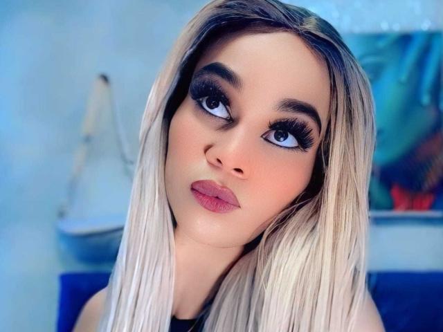KateHadid has blonde hair, blue eyes, thick black eyelashes, and pink lipstick. She's looking up with a pouty expression. Her tits are not visible.