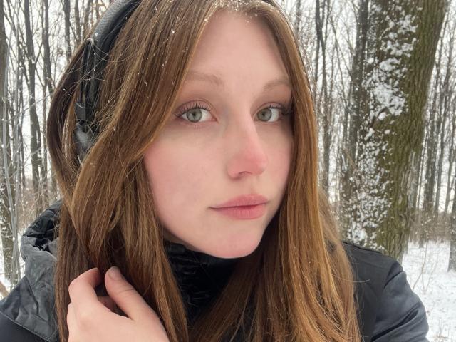 MelinaBoye has pale skin, green eyes, and brown hair with snowflakes in it. She's wearing black headphones and a black jacket, looking slightly annoyed. Her ass is not visible.