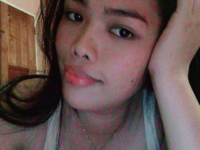 EvaBuntog with pouty lips, brown eyes, and a small mole on her left cheek, wearing a white tank top, touching her head with her right hand.