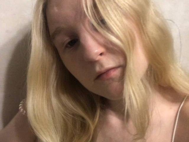 HyacinthBellin has blonde hair, slightly parted, covering one eye, with a neutral expression, pale skin, and wearing a thin-strapped top. Her face is centered in the image.